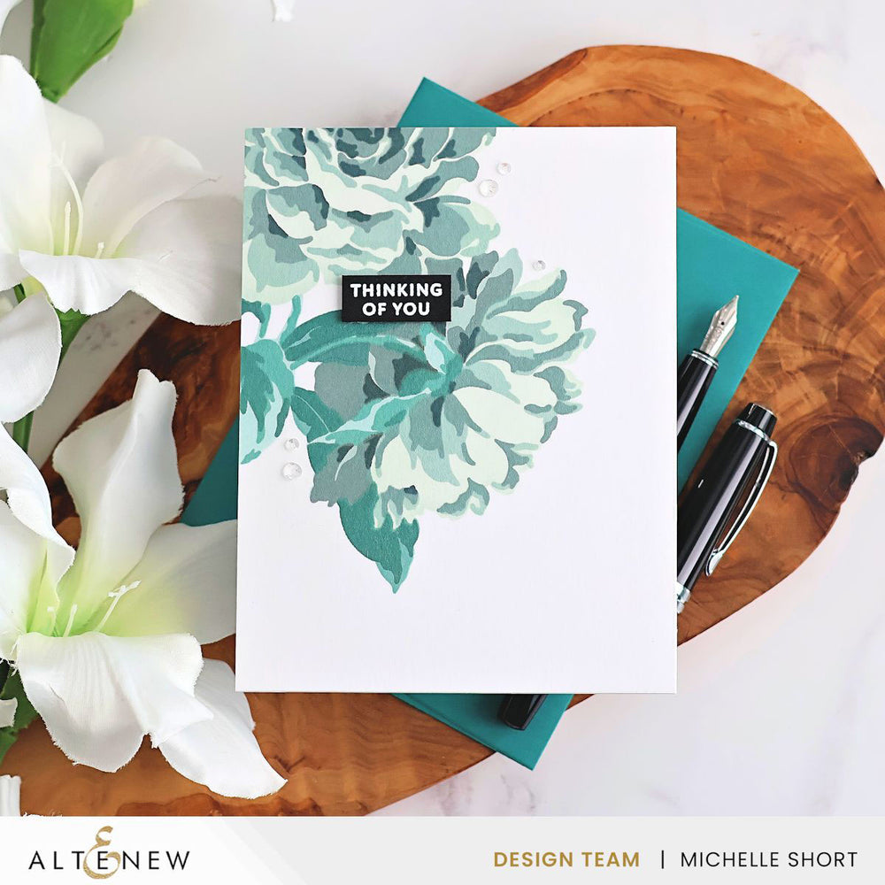 Floral card with 'Thinking of You' message on a wooden surface with flowers and pens.