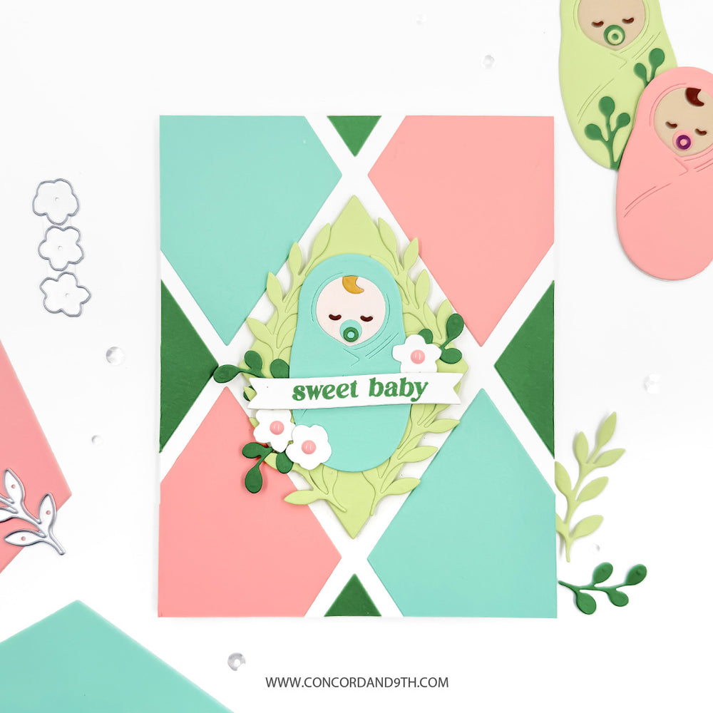 A card made with the Concord & 9th Bloom & Grow set: a swaddled baby in a leafy wreath with 'sweet baby' on a pink and mint diamond background.