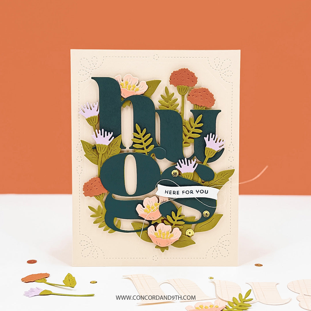 A card made with the Concord & 9th Floral Embrace set: a large dark teal 'hugs' surrounded by pink, coral and lilac flowers, with 'here for you'.
