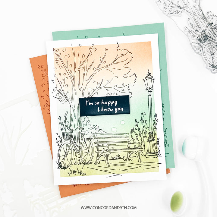 A card made with the Concord & 9th Park Bench set: a stamped park scene with a bicycle and bench on a peach to mint background, and 'I'm so happy I know you'.