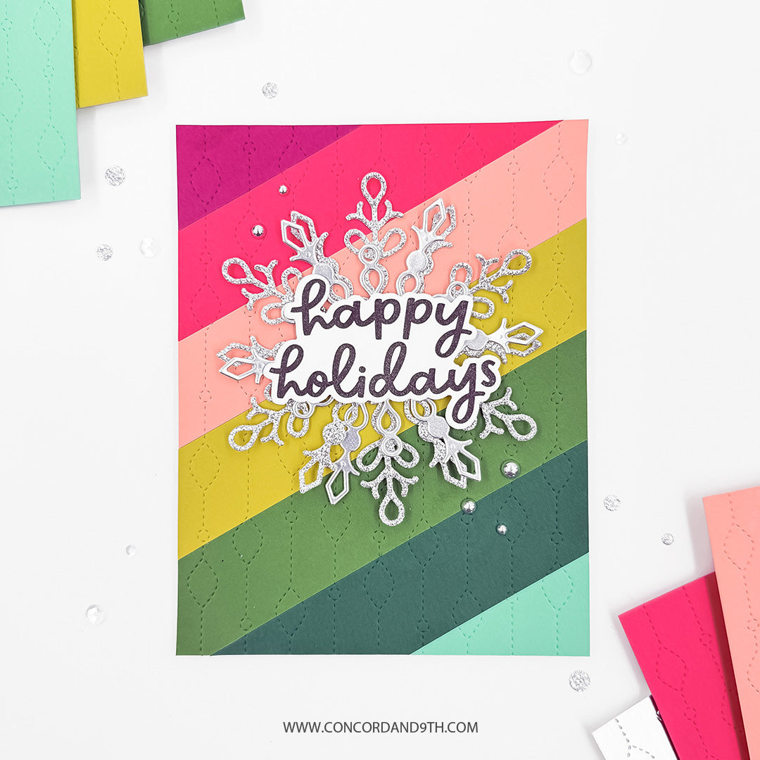 Concord & 9th Chandelier Card Front Die — a rainbow-striped card front cut in the die's repeating diamond-and-teardrop pattern, with a die-cut snowflake and "Happy Holidays" sentiment.