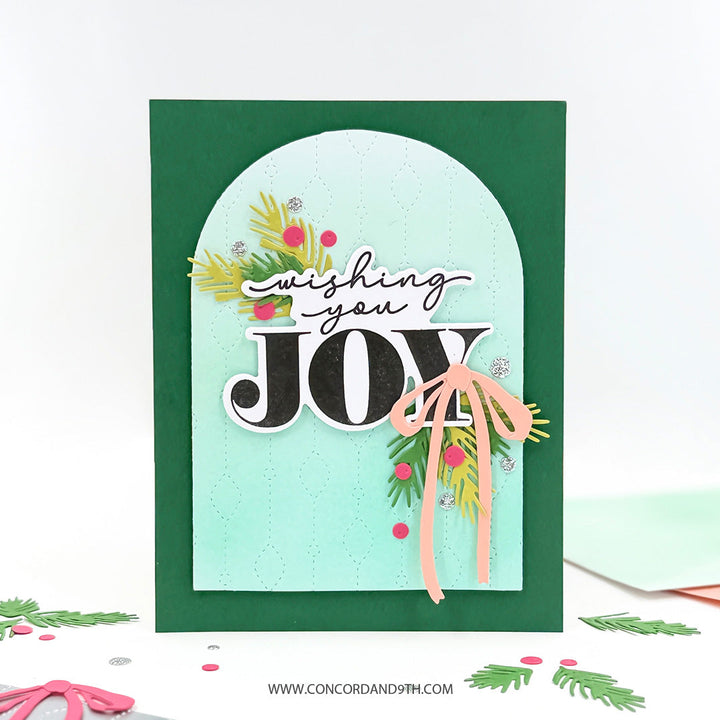 Concord & 9th Chandelier Card Front Die — the repeating bead pattern on a mint arch panel over a dark green card, with pine sprigs, a bow and a "Wishing You Joy" sentiment.