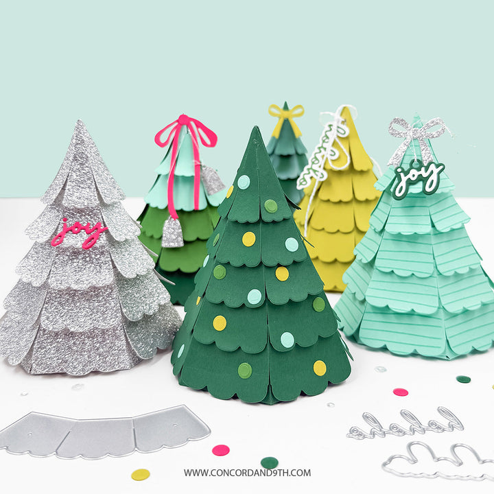 Concord & 9th Evergreen Box Dies — a row of 3D pyramid gift boxes in silver, sage, dark green with dot ornaments, yellow, and mint striped cardstock, each topped with a bow and hanging tag.