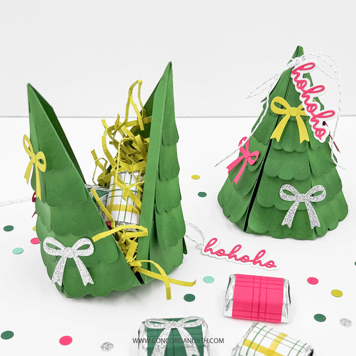 Concord & 9th Evergreen Box Dies — one box opened and filled with shredded paper and a wrapped treat, another closed with a glitter bow and "hohoho" tag, with mini wrapped candy favours.