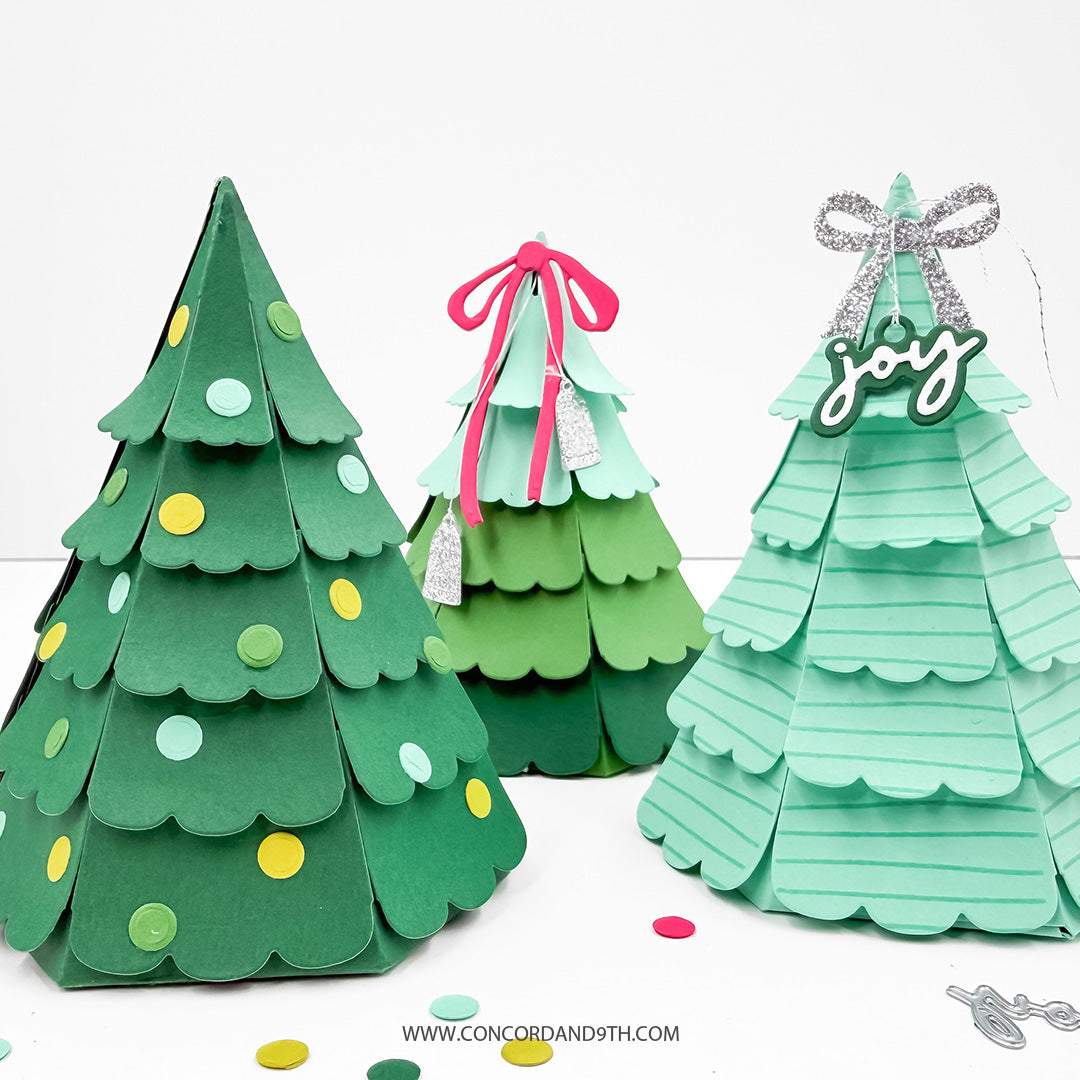 Concord & 9th Evergreen Box Dies — the die-cut scalloped tree panel and an assembled dot-ornament box, with loose bows, sentiment tags and confetti.