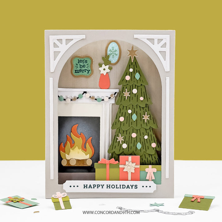 Concord & 9th Holiday Home Dies — a dimensional shadow-box card with an arched mantel scene: fireplace, decorated tree, gifts and wall art, with a "Happy Holidays" sentiment strip.