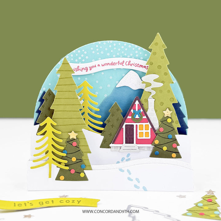 Concord & 9th Into the Woods Dies — a dimensional card with an A-frame cabin scene, decorated trees and a snowy mountain backdrop, with a "wishing you a wonderful Christmas" banner.
