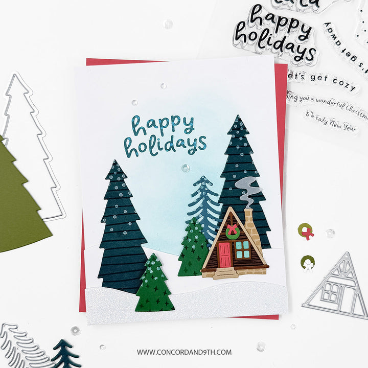 Concord & 9th Into the Woods Dies — the cabin and layered pine tree scene in a snowy landscape, with a "happy holidays" sentiment.