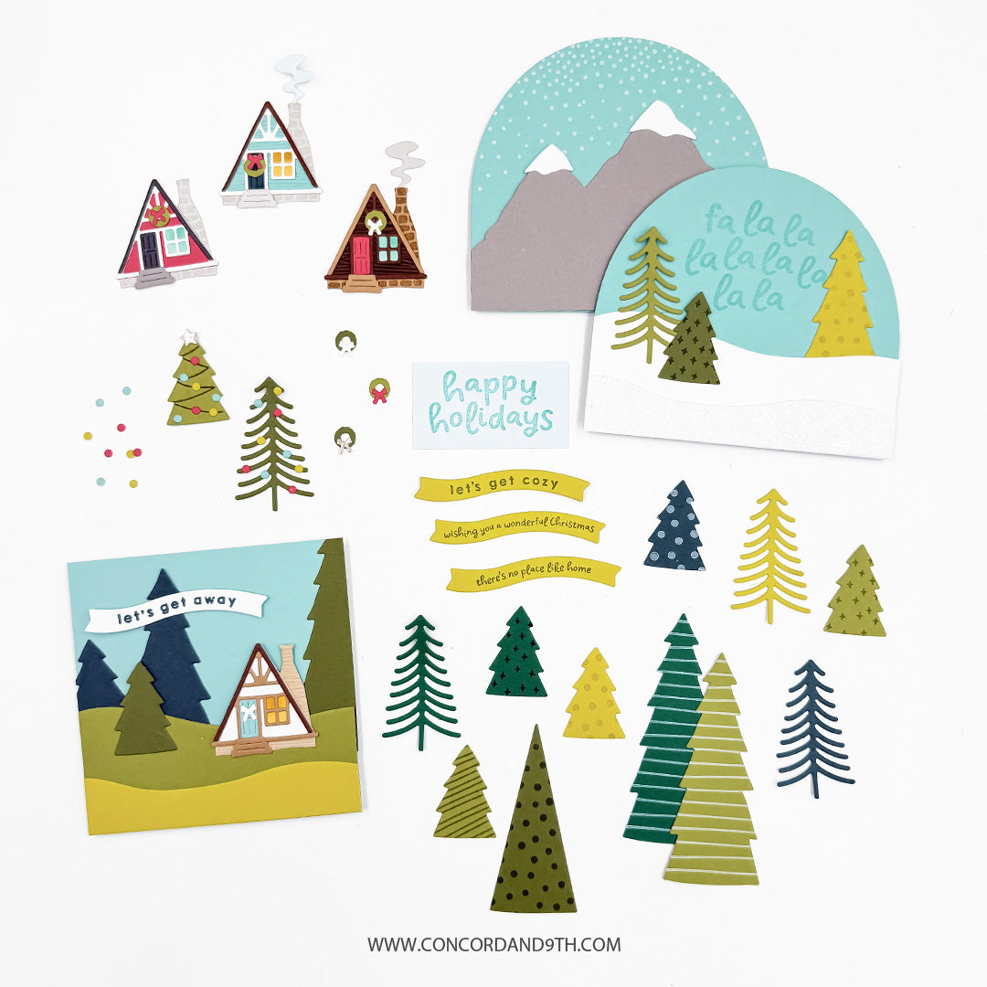 Concord & 9th Into the Woods Dies — several A-frame cabins, patterned trees, snow-globe-style scene panels, and sentiment banners like "let's get cozy" and "there's no place like home."