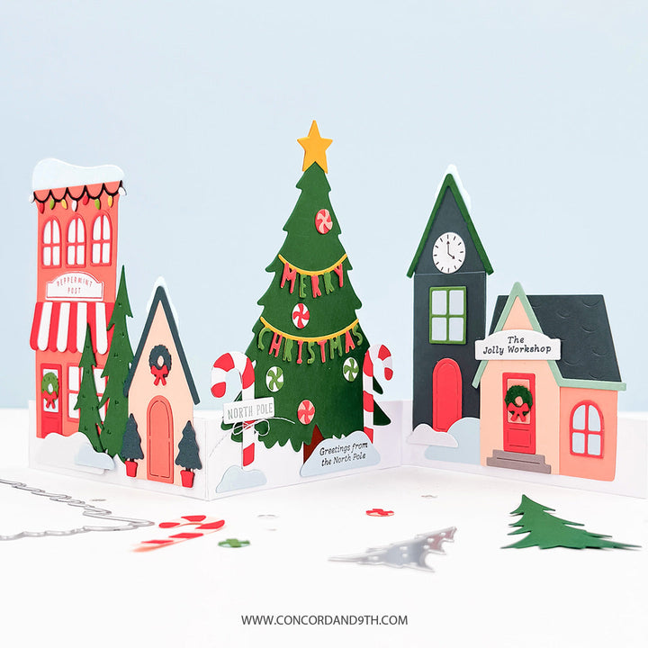 Concord & 9th North Pole Greetings Bundle — a dimensional card with a row of North Pole village shop-fronts including "Peppermint Post" and "The Jolly Workshop," a candy-striped tree and "Merry Christmas" banner.