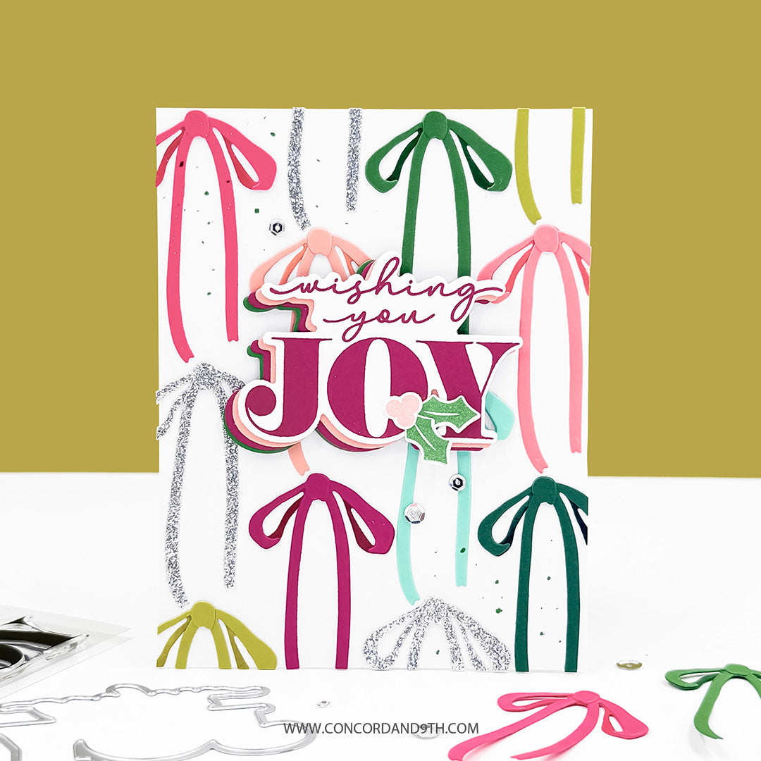 Concord & 9th Tidings of Joy Dies — a card layered with colourful ribbon die-cuts and a "wishing you JOY" sentiment.