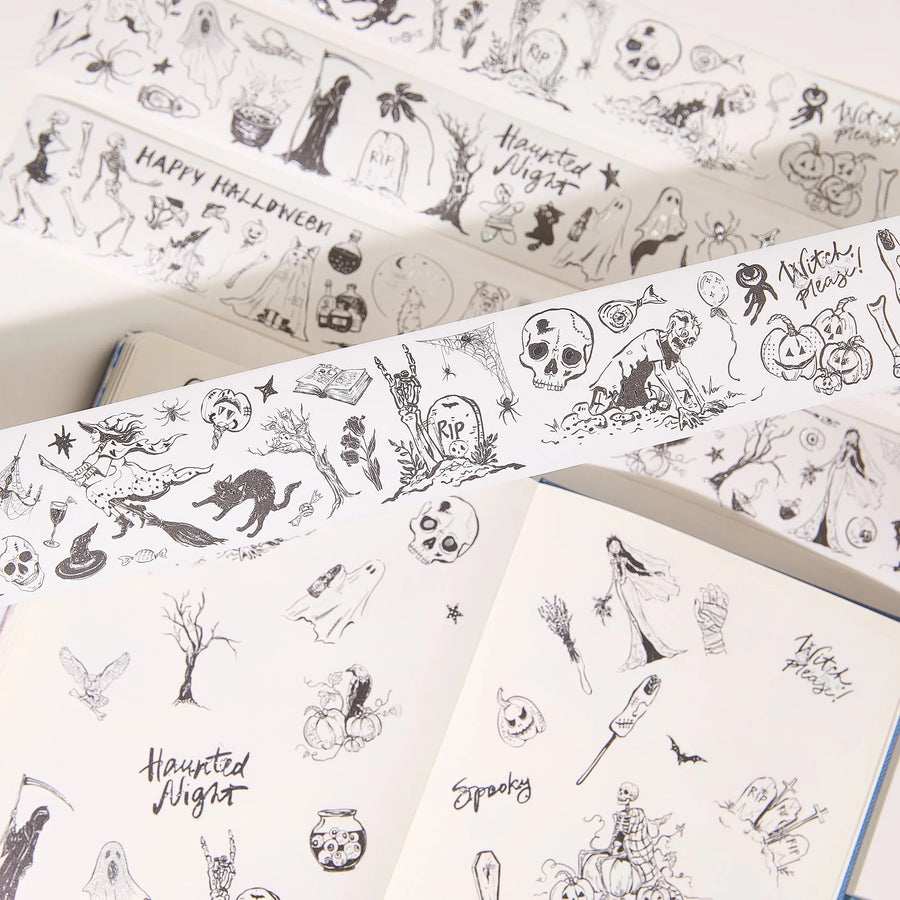 Halloween-themed washi tape rolls with black line-art illustrations of skulls, ghosts, pumpkins, bats, and spooky text, shown partially unrolled over open notebooks.
