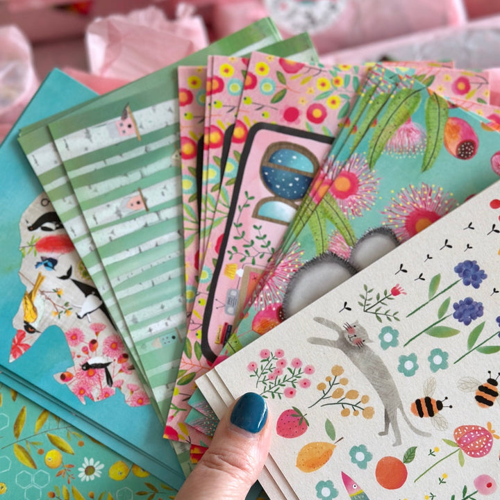 Colourful postcards in hand with various designs by Kate Mason Art