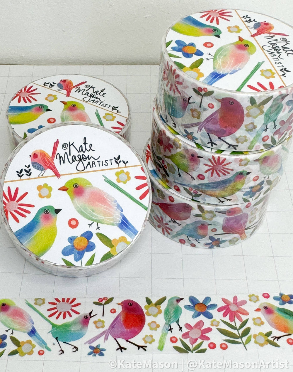 Colourful washi tape rolls with birds and floral designs by Kate Mason on a white surface.