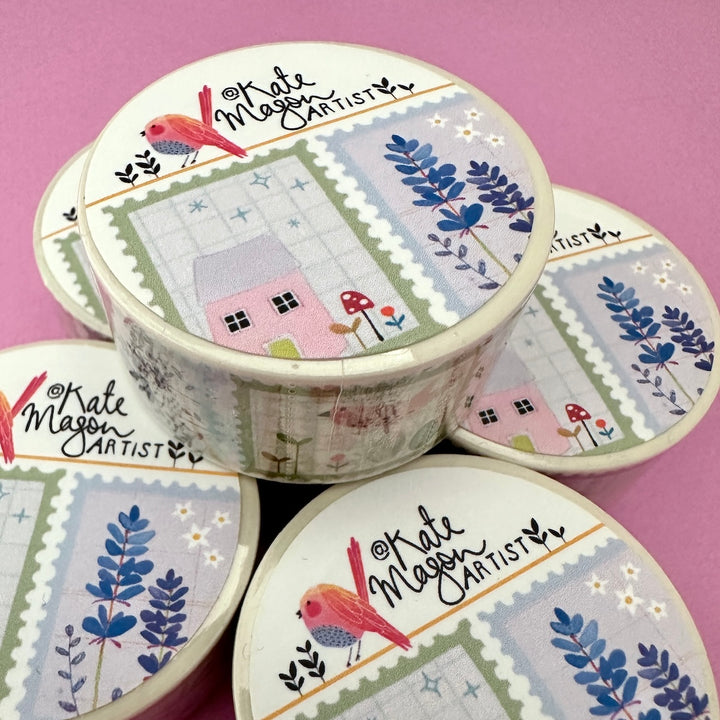 Washi tapes arranged on a pink background. The lids show a patchwork design with blue flowers, a small pink house, red mushrooms, and the text 'Kate Mason Artist'.