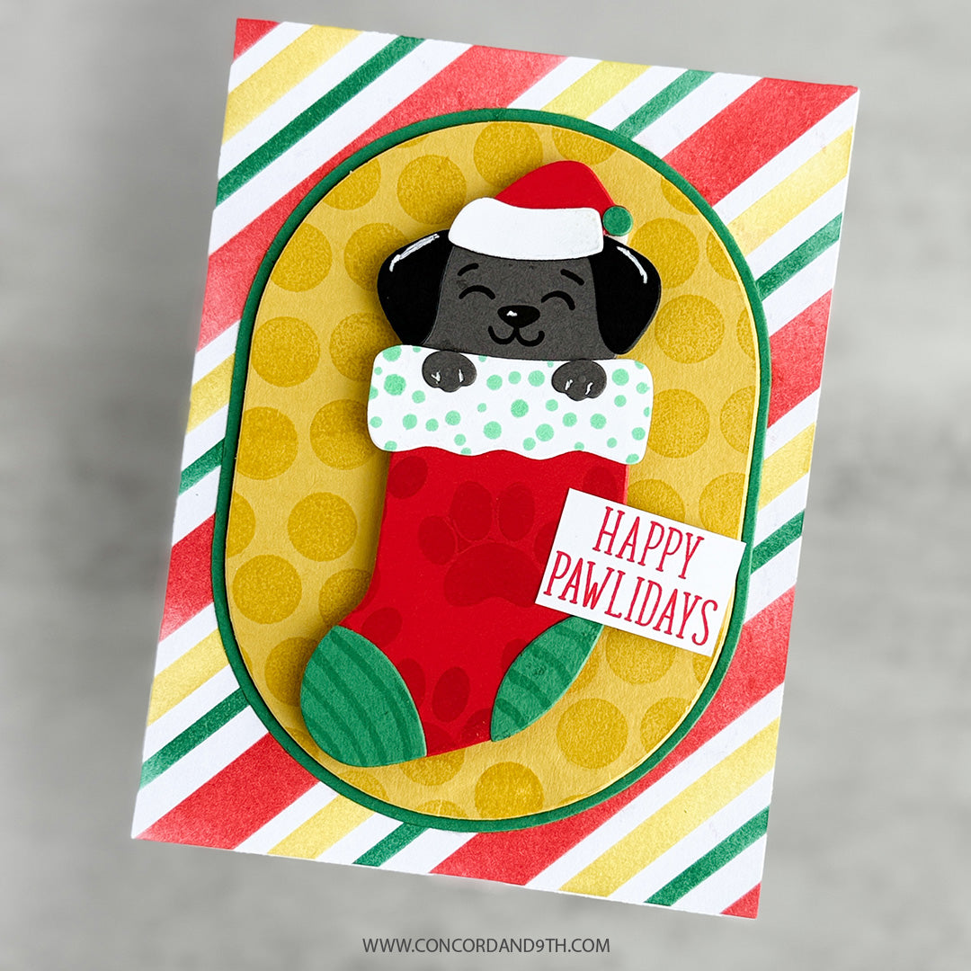 A card made with Kristina Werner's Happy Pawlidays Dies: a black puppy in a Santa hat sits in a red stocking with 'Happy Pawlidays' on bright stripes.