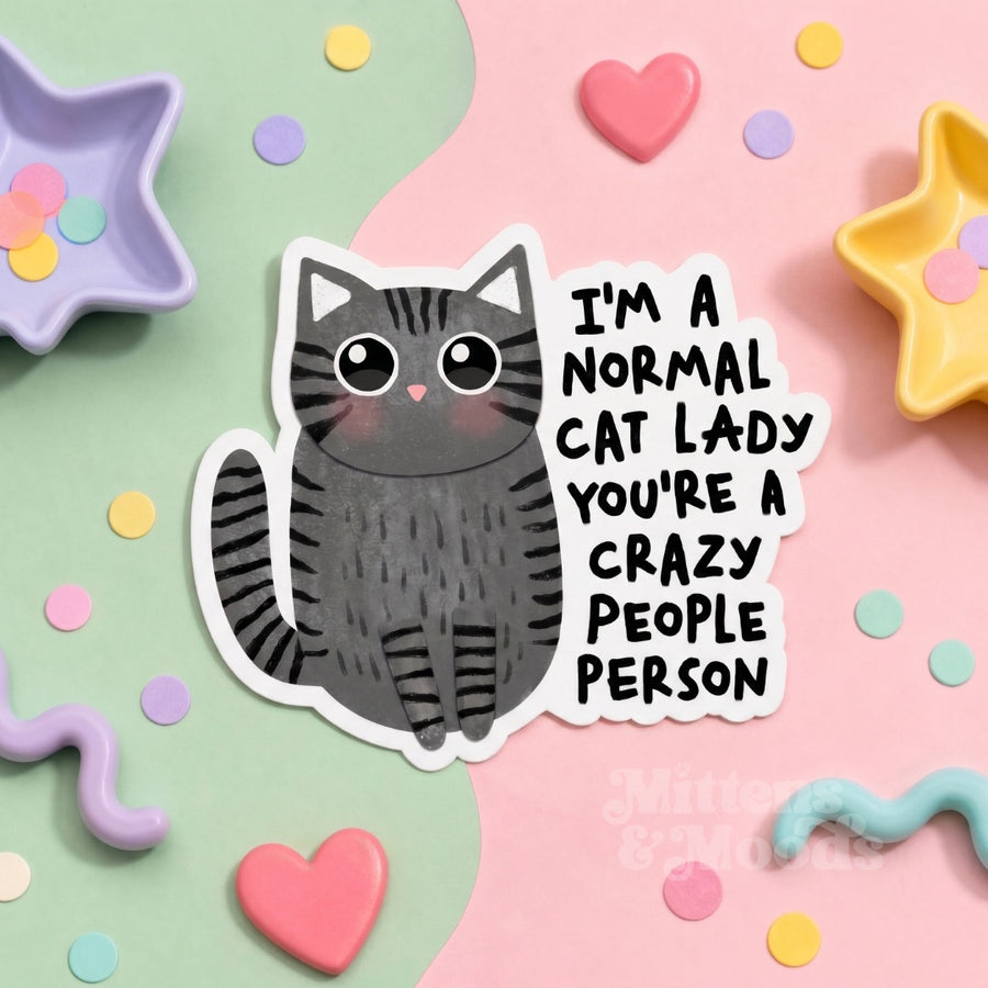 A die-cut sticker featuring a cute cartoon gray tabby cat next to the text 'I'M A NORMAL CAT LADY YOU'RE A CRAZY PEOPLE PERSON' in black handwritten-style lettering. The sticker is displayed on a pastel pink and mint green background decorated with colorful confetti, star-shaped dishes.
