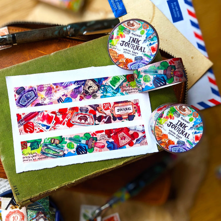 A styled flat-lay of a washi tape product called 'Ink Journal'. The product is a colorful retro-themed washi tape (depicting stamps, candy, and postcards) shown unrolled on an olive green notebook, alongside two round matching tape rolls.
