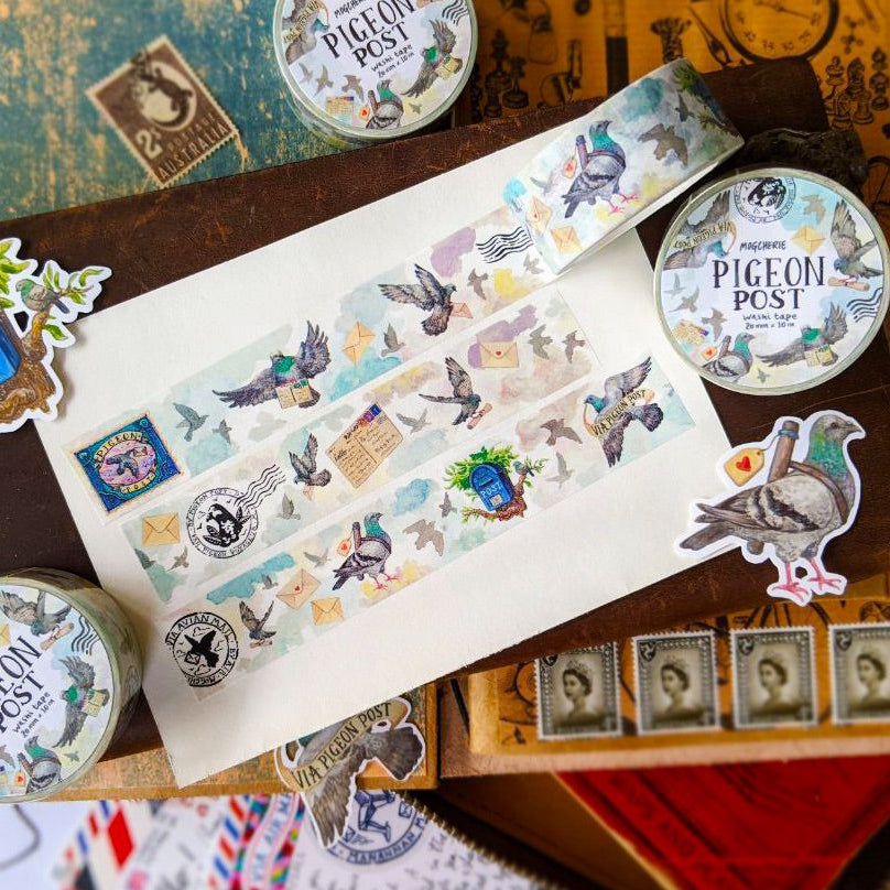 A styled flat-lay of 'Pigeon Post' washi tape featuring illustrated pigeons, stamps, and postmarks, arranged on a vintage wooden box with matching stickers and tins.