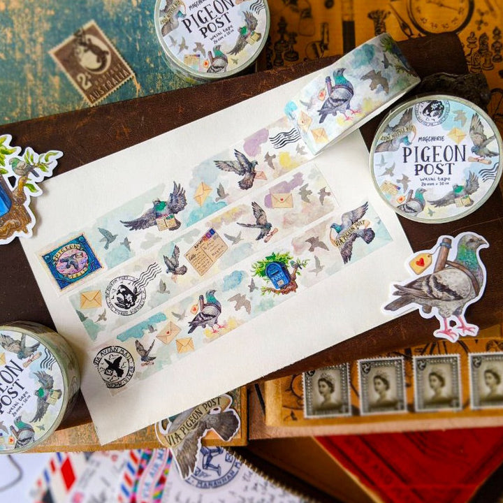 A styled flat-lay of 'Pigeon Post' washi tape featuring illustrated pigeons, stamps, and postmarks, arranged on a vintage wooden box with matching stickers and tins.