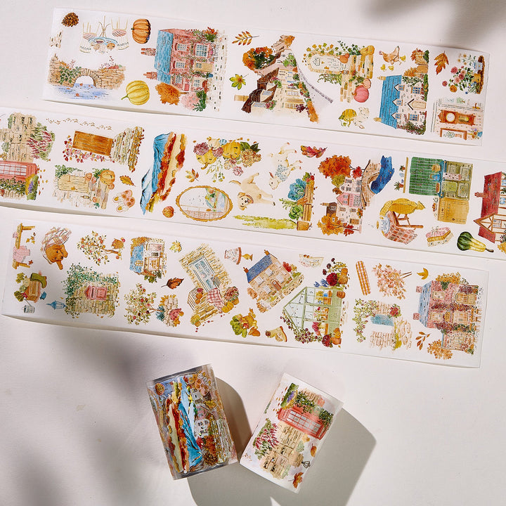 Strips of The Washi Tape Shop Autumn Village Wide Washi/PET Tape laid flat with the rolls, showing the full design