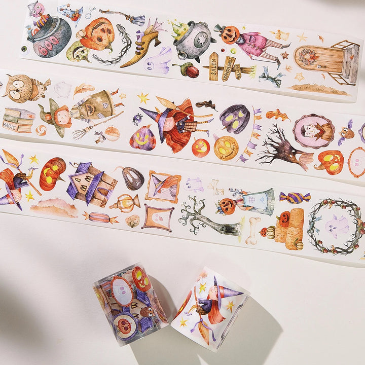 Three strips of decorative washi tape with colourful Halloween illustrations are arranged on a white surface, with two rolls placed in front. The tape features whimsical autumn and spooky motifs including pumpkins, ghosts, owls, haunted houses, and autumn leaves in pastel and bright watercolour style colours.