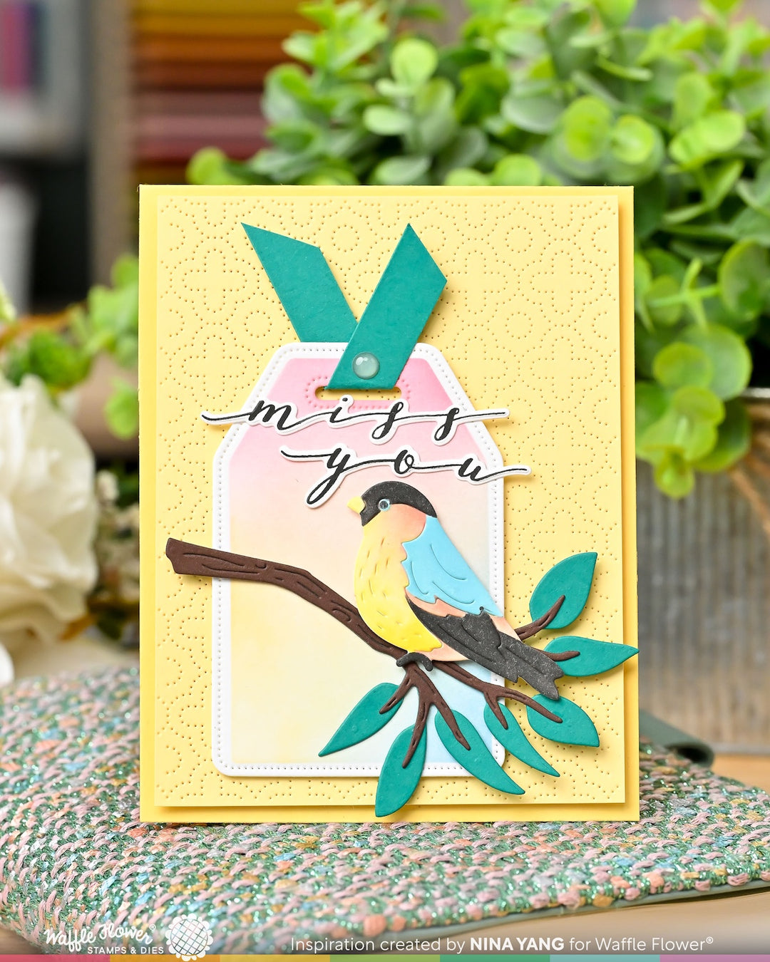 Card with bird design and 'miss you' text on a yellow background, with plants in the background.