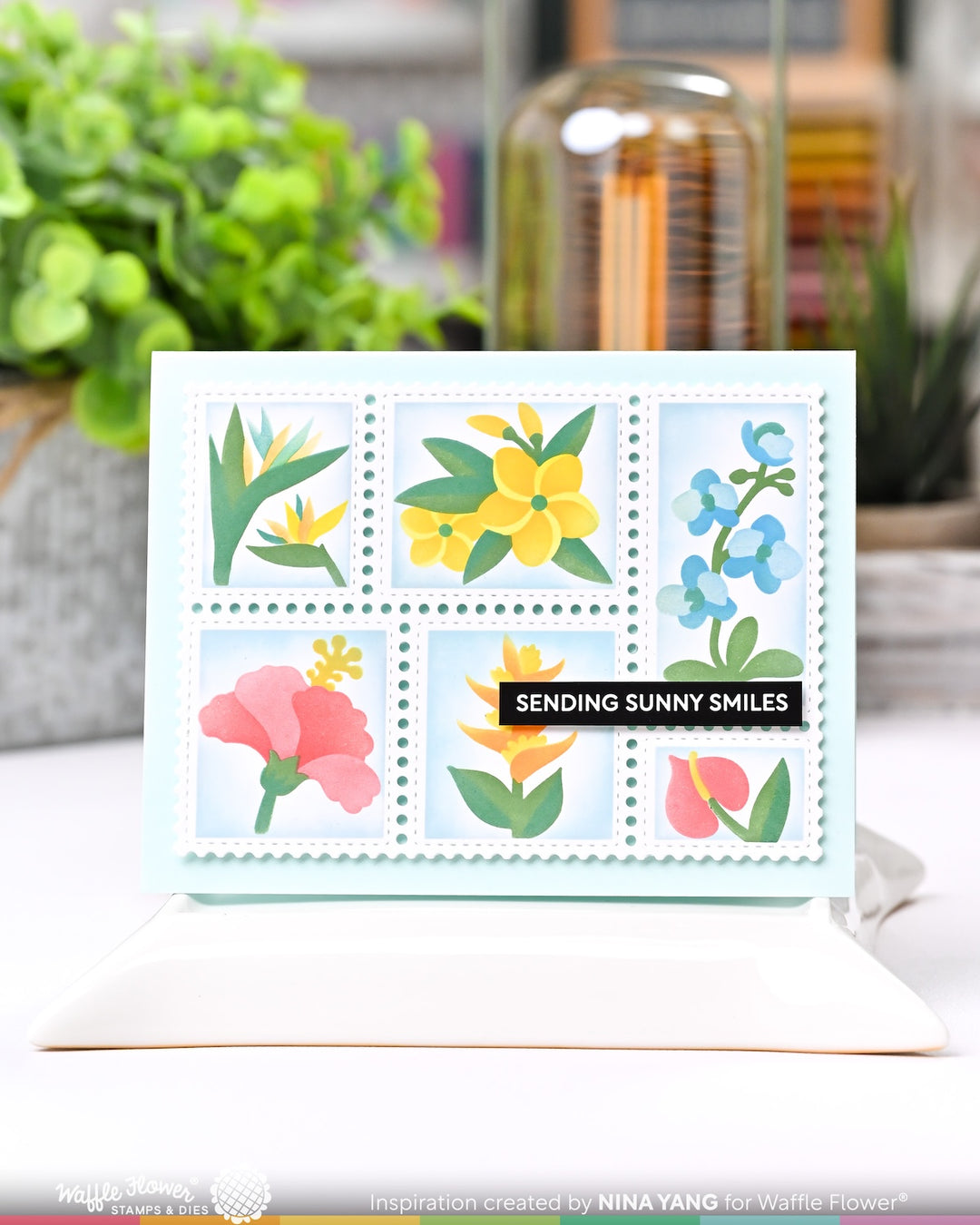 Postage collage Card with floral design and 'Sending Sunny Smiles' text on a blurred indoor background