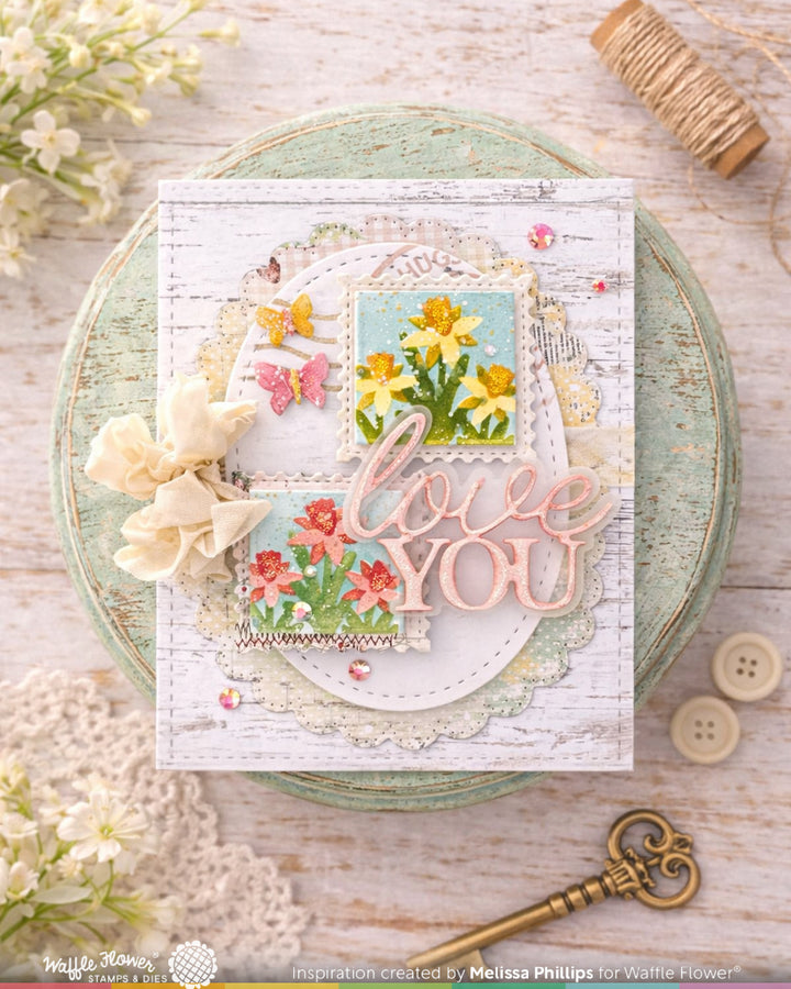 Decorative card with floral designs and 'love you' text on a wooden surface with flowers and buttons.