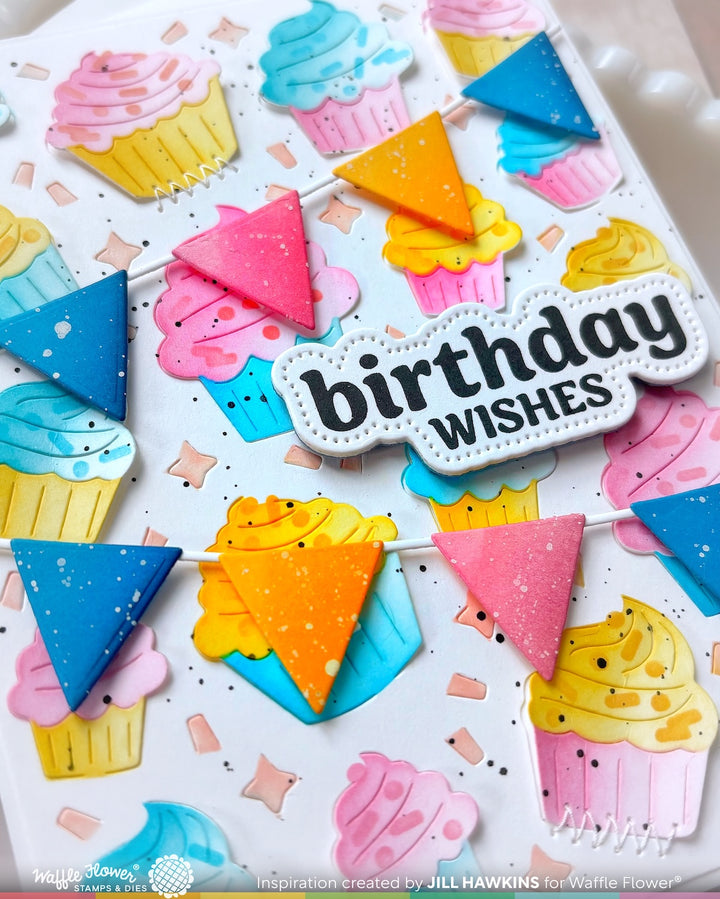 A close-up of a handmade birthday card featuring colorful cupcake illustrations, bunting flags, and a central white die-cut label that reads 'birthday WISHES'.