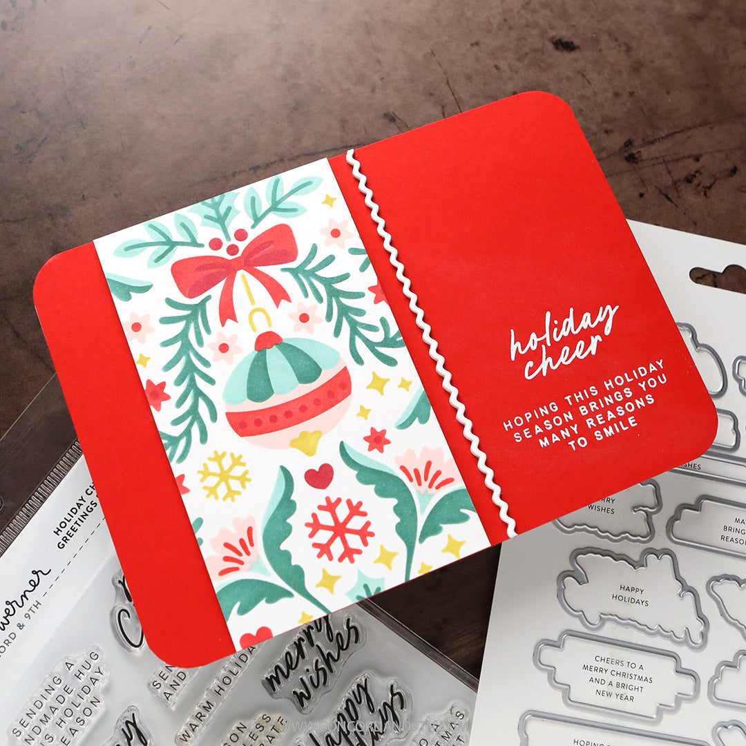 Concord & 9th Kristina Werner Holiday Cheer Greetings Stamps — a red card with a folded ribbon edge and a stamped ornament and floral illustration.