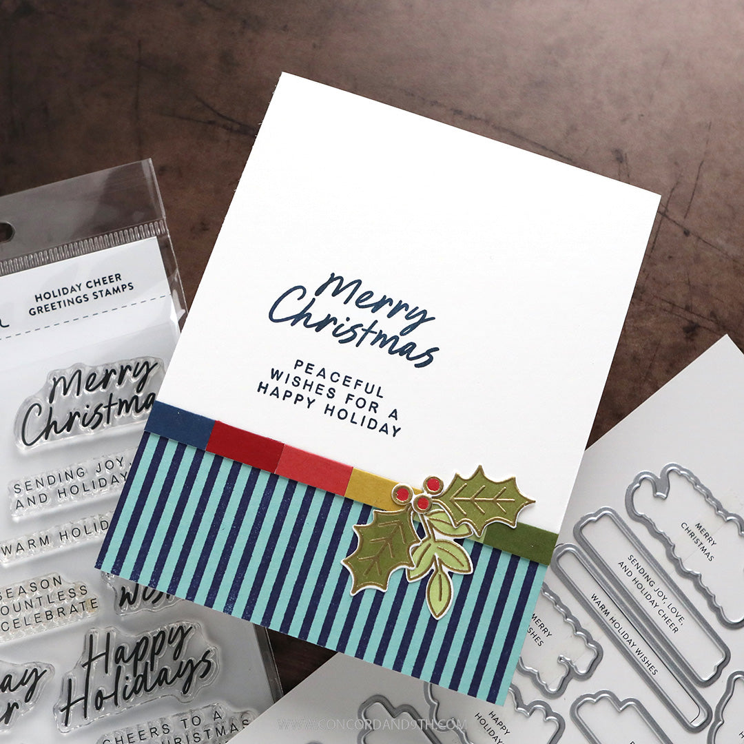 Concord & 9th Kristina Werner Holiday Cheer Greetings Bundle — a "Merry Christmas, Peaceful Wishes" card with a stamped holly sprig, shown with the coordinating stamps and dies packaging.