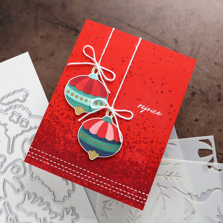Concord & 9th Kristina Werner Ornamental Christmas Dies — a red "rejoice" card with two hanging die-cut ornaments and a speckled background.
