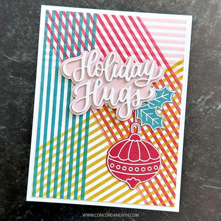 Concord & 9th Kristina Werner XL Basic Stripes Background Stamp — a plaid-striped "Holiday Hugs" card with a stamped holly sprig and ornament.