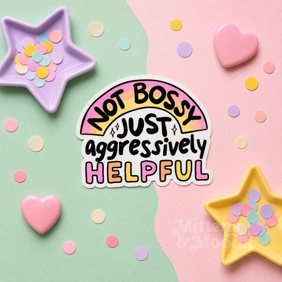 A die-cut sticker with the text 'NOT BOSSY JUST aggressively HELPFUL' in black and pastel pink, yellow, and purple lettering, placed on a pastel split background with star-shaped confetti dishes.
